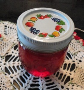 1/2 pint, sealed canning jar; white screwband/fruit ring on lid; white doily, strawberry jelly, jelly
